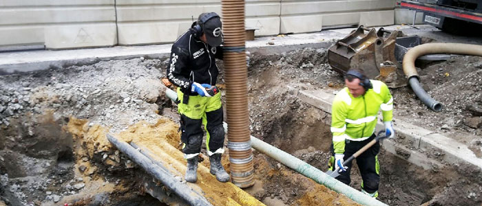 Medarbetare från Sundbyberg Avfall och Vatten står i ett schakt i marken
