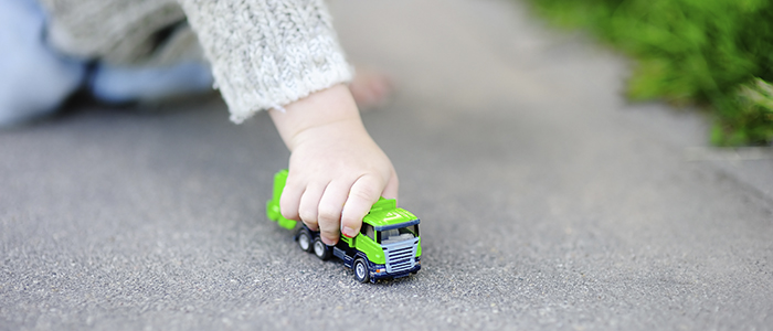 Ett barn sitter på marken och leker med en grön leksakssopbil