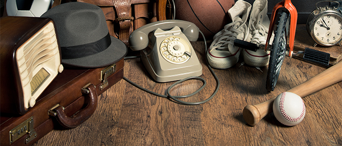 En samling med antika saker. Det är en portfölj, en radio, en hatt, en telefon, ett par basketskor, en trehjuling med mera