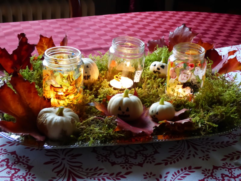 På en röd duk står ett silverfat med dekorerat med halloweenljusstakar, små dekorationspumpor, mossa och höstlöv
