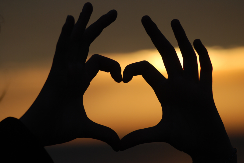Händer formar ett hjärta i solnedgången