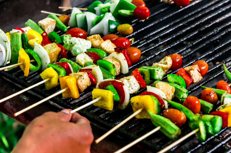 Grillspett med paprika, lök, bröd och tomat ligger på rad på ett grillgaller.