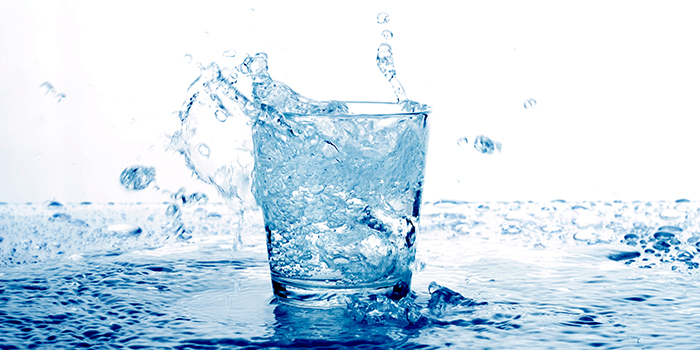 Ett vattenglas fyllt med vatten som är i rörelse och svämmar över. Glaset står i vatten