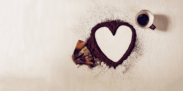 Ovanpå en bänkskiva ligger det ett använt kaffefilter och kaffepulver ligger utspritt i formen av ett hjärta. Bredvid står det en nästan urdrucken kaffekopp.