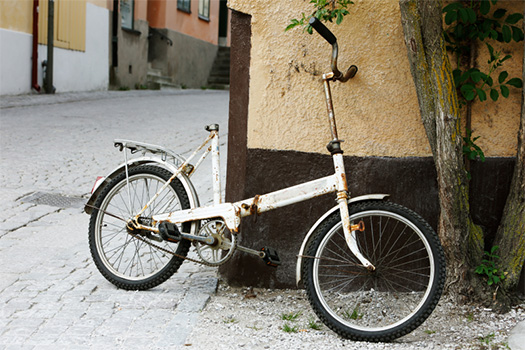 En trasig cykel som saknar sadel står lutad mot en husfasad