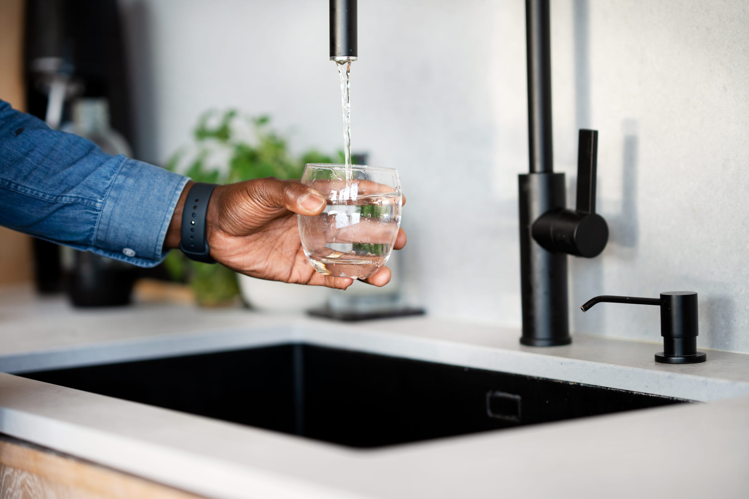 En hand håller in ett glas under en vattenkran. Vattnet fylls på i glaset