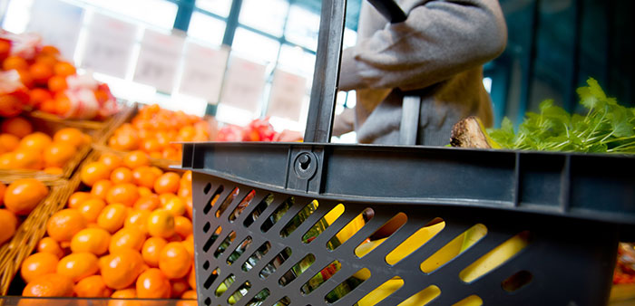 Avdelning för frukt och grönt i en mataffär. I förgrunden en kundkorg, i bakgrunden clementiner och apelsiner.