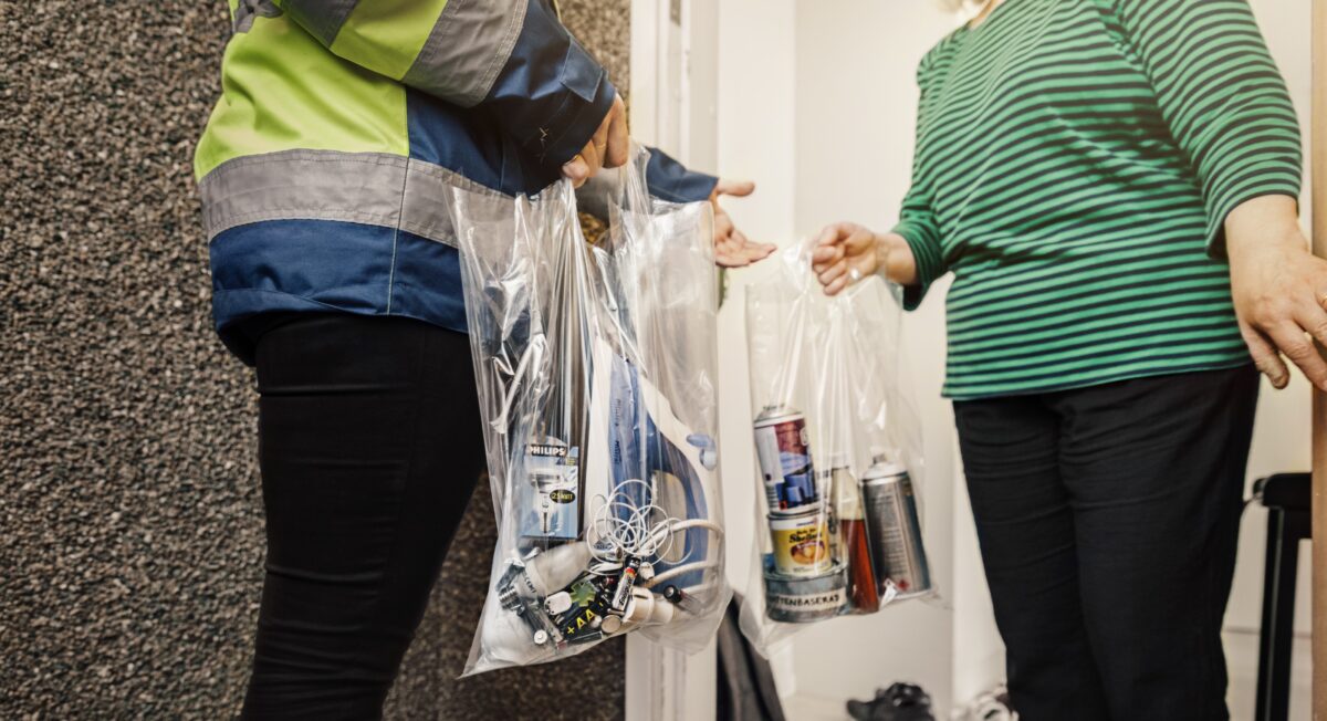 En kvinna överräcker två plastpåsar innehållande el-avfall och farligt avfall vid sin dörröppning, till personal från Savab som hämtar.