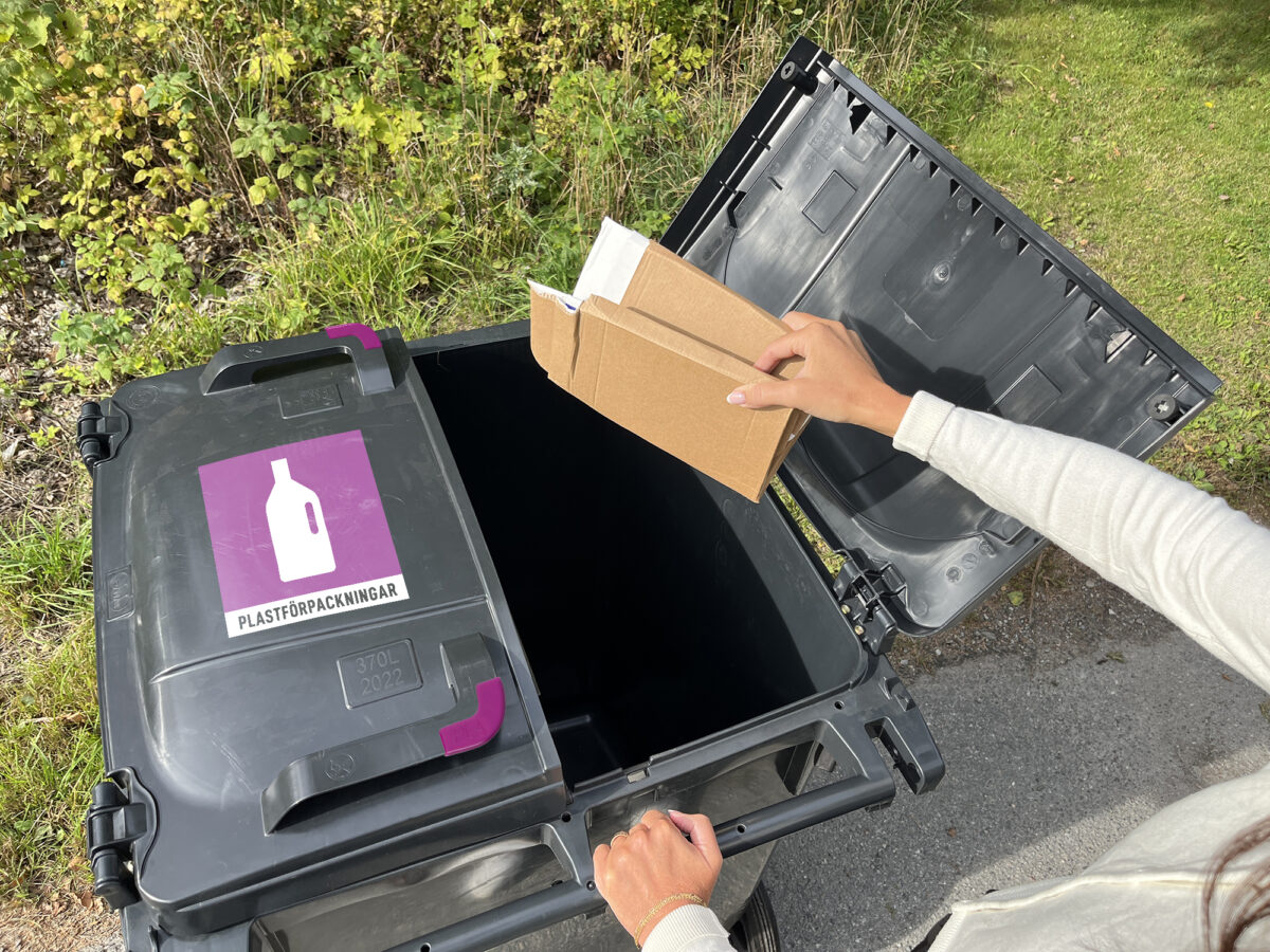 En kvinna håller i en pappersförpackning som hon ska slänga i tvåfackskärlet för pappers- och plastförpackningar.
