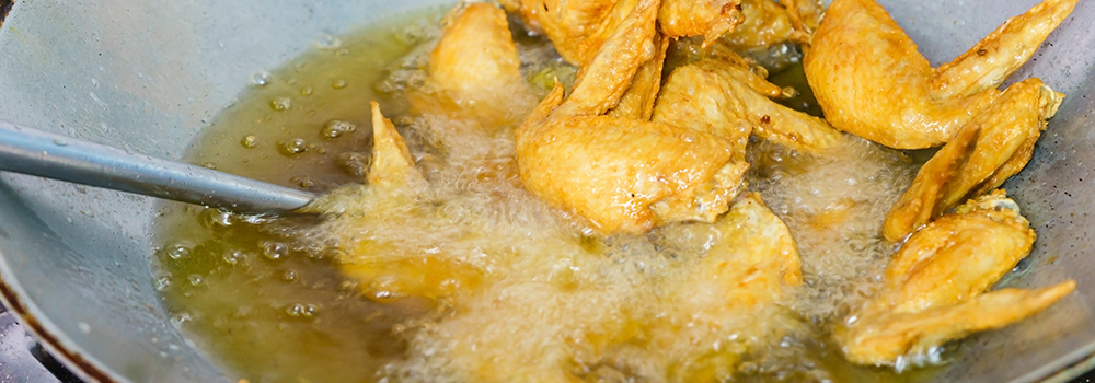 En wokpanna fylld med frityrolja och kycklingben